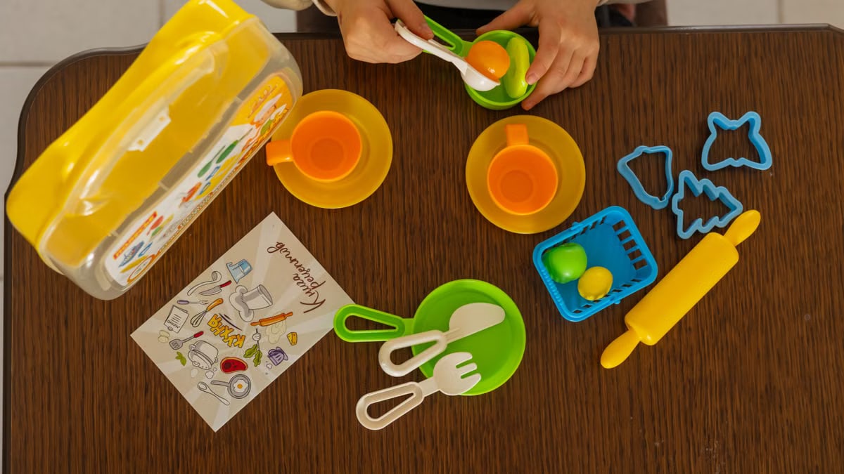 A child is engaging in creative play with a vibrant toy kitchen set on a wooden table.