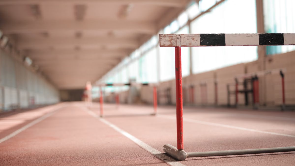 Hurdle painted in white black and red colors placed on empty rubber running track in soft focus